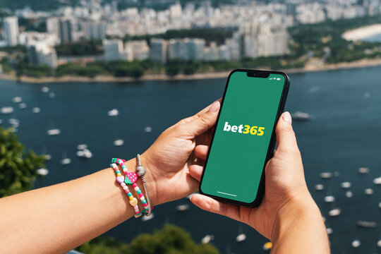 Girl holding smartphone with Bet365 betting provider app on screen. City and bay with some boats in the background. Rio de Janeiro, RJ, Brazil. November 2022