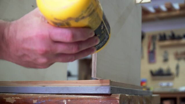 Carpenter applying PVA glue to wood to make a musical instrument in a workshop