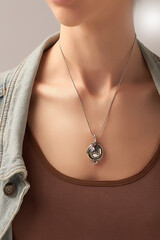 Cropped shot of a lady wearing a metal silver necklace made out of a chain with a dangling pendant...