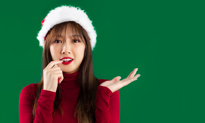 Merry Christmas, young asian woman in red sweater wearing santa hat looking camera hand pointing copy space green screen background. - Powered by Adobe