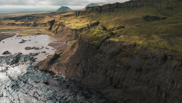 Aerial rise over dramatic, rugged Iceland mountain landscape, melting glacier.