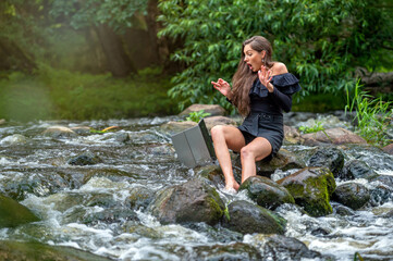 female freelancer sitting on a rock in the river and dropping her laptop into the water