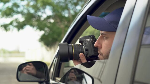 private detective sitting inside car taking picture with professional slr camera