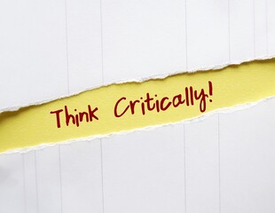 Torn yellow paper with handwritten text THINK CRITICALLY! to remind self to focus on logical and...