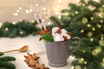 Hot chocolate with marshmallows and christmas cookies.  
Fir tree branches with lights in the...