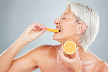 Beauty, orange and eating with a mature woman biting into a fruit slice in studio on a gray...