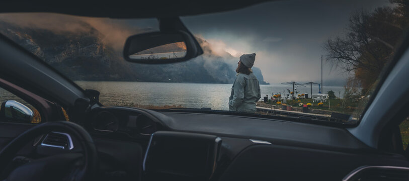 Young woman driver traveler enjoying lake view on foggy autumn day, view through car