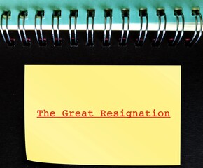 Yellow note stick on notebook with red text THE GREAT RESIGNATION, ongoing trend of the big quit,...