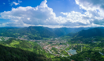 Fototapeta premium Bulgarian town Smolyan with lake, vegetation and clouds. Rhodope Mountains. Panorama, top view
