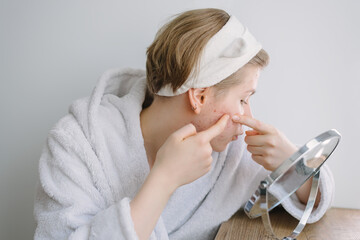 Acne. A teenage girl looks in the mirror at her problematic skin and squeezes out pimples. Problem...