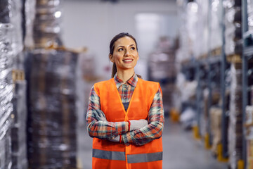 A happy warehouse blue collar worker is standing with arms crossed in facility.