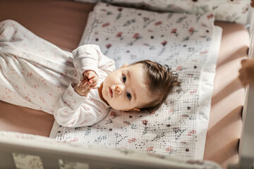 Portrait of a baby girl lying in her crib and looking at the camera.