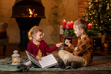 Siblings reading book fairy tales Christmas and New Year evenings at cosy candle home. Concept of...