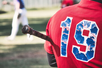 Close-up of the back of a baseball player holding a bat with the number 19 on a red shirt team uniform