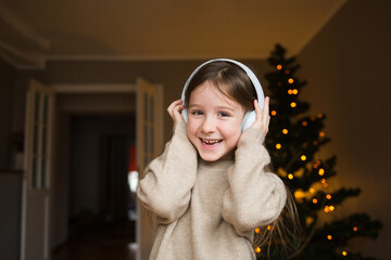 happy child in headphones listening to music and dances on background of Christmas tree at home