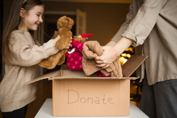cardboard box with inscription donate. family mother and child put clothes and toys in box at home...