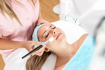 Beautician therapist applying face treatment in beauty salon to young woman.