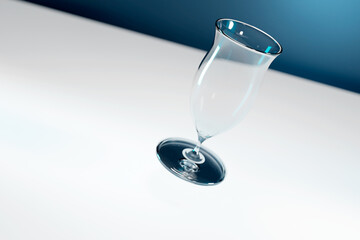 Empty single levitating and tilted tulip shaped beer glass on navy blue and white background.