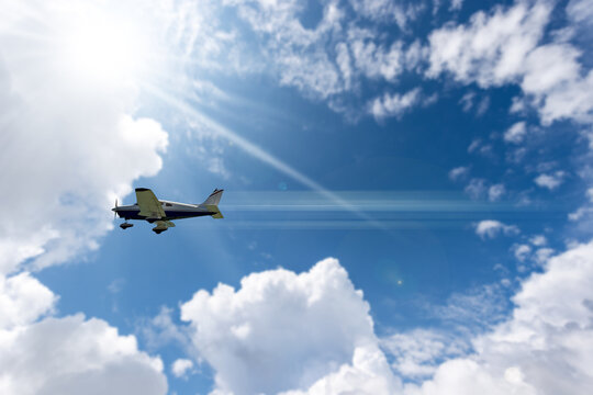 Small private propeller airplane in motion against a beautiful clear blue sky with cumulus clouds and sunbeams.
