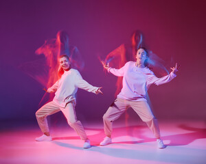 Portrait of two young girls training, dancing hip-hop isolated over gradient violet background in neon with mixed light