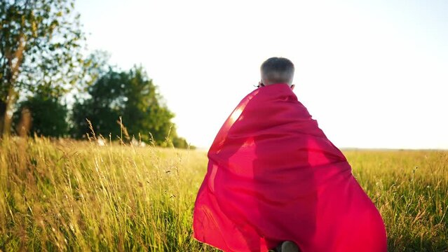 baby superhero run. happy family kid dream concept. a small child in a mask and a red raincoat runs along the path in nature in the park plays a superhero. top dreamer fun baby run