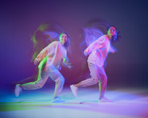Portrait of young girls dancing hip-hop isolated over gradient blue purple background in neon with mixed light. Looking happy
