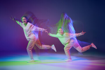 Portrait of young sportive girls dancing hip-hop isolated over gradient blue purple background in neon with mixed light.