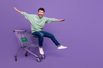 Full size portrait of positive crazy person sit market trolley arms wings isolated on purple color...