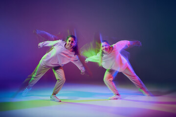Portrait of young girls dancing hip-hop isolated over gradient blue purple background in neon with mixed light. Dance club