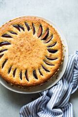 Overhead view of a homemade frangipane plum tart, served on a rustic table with a striped napkin. Delicious seasonal dessert with almonds and plums