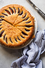 Overhead view of a homemade frangipane plum tart, sliced and served on a rustic table with a striped napkin. Delicious seasonal dessert with almonds and plums.
