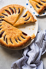 Overhead view of a homemade frangipane plum tart, sliced and served on a rustic table with a striped napkin. Delicious seasonal dessert with almonds and plums.