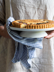 Freshly baked frangipane and plum cake with female holding the cake with a striped tea towel