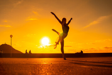 Fototapeta na wymiar Silhouette of a young woman dancer by the beach at sunset raising her leg