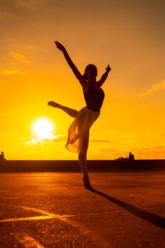Silhouette of a young woman dancer by the beach at sunset doing an acrobatic