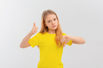 Serious teen girl, frowns and points thumbs up and down with disappointed face expression, stands in casual yellow t shirt over white background