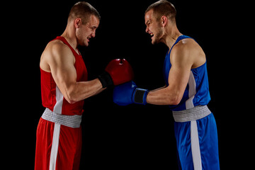 Fototapeta na wymiar Greeting rival. Two twins brothers, professional boxers in blue and red sportswear boxing isolated on dark background.