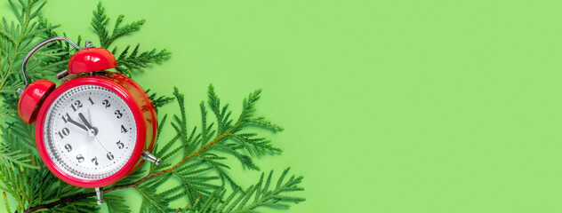 Alarm clock  with tree branches on green paper background. 5 minutes before the New Year. Creative greeting card