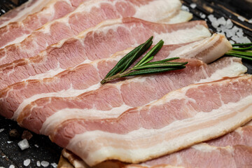 Close up Bacon slices. Pig meat. Pork belly with rosemary on a wooden board, Keto diet food ingredients. Restaurant menu, dieting, cookbook recipe