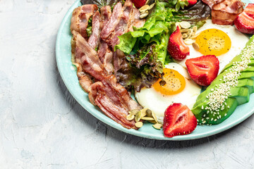 Ketogenic diet food, Fried egg bacon with avocado, strawberries and fresh salad on a light background. healthy meal concept, Long banner format. top view