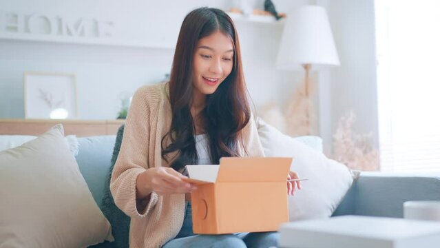 Excited young asian woman unpacking carton box and looking inside, Emotional female surprised by fast delivery service, Happy woman client satisfied with ordered purchase, Online shopping.