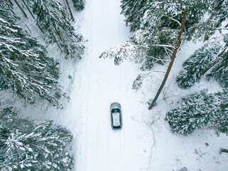 Drone shot of a car driving on a snowy road in the middle of a forest of pine trees in winter