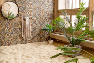 Room decorated in boho style with green tropical plants and sand on floor