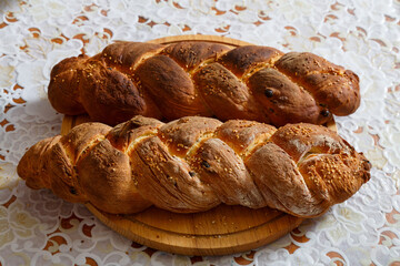 Freshly baked challah with sesame seeds for Shabbat on a wooden board on a white tablecloth.