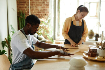 Side view portrait of young black man shaping clay while enjoying art class in pottery studio, copy...