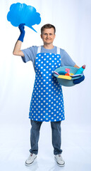 male housewife in blue apron, rubber gloves, blue t-shirt, jeans. the housekeeper holds a bowl of...