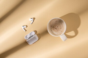 Cappuccino, wireless headphones on a beige background. Flat lay, top view.