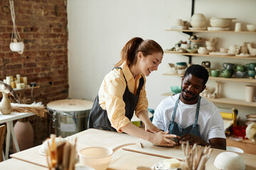 Warm toned portrait of smiling multirational couple making handmade ceramics in pottery studio...
