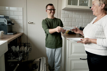 Caucasian adult man with down syndrome and his mother unloading dish washer at home