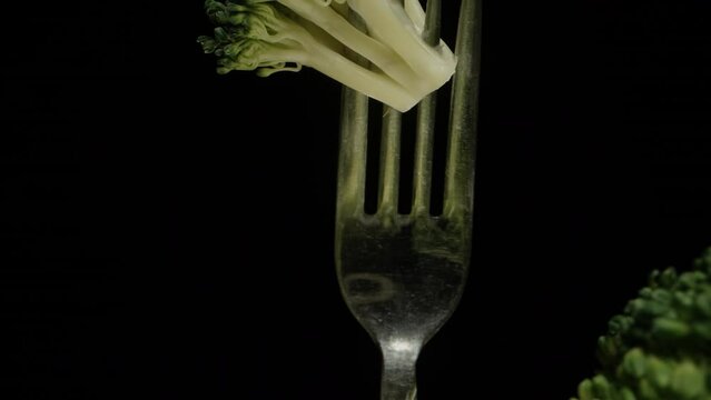Broccoli on a fork rotates on a black background. Dolly slider extreme close-up.